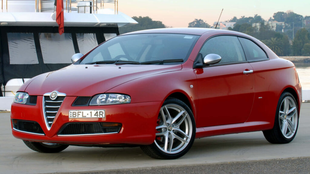 Red Alfa Romeo GT parked by water with sleek sporty design in sunlit scenic wallpaper background