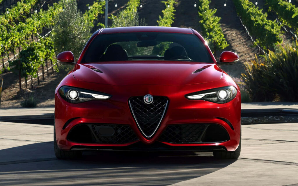 Red Alfa Romeo Giulia driving on scenic mountain road with lush vineyards background wallpaper
