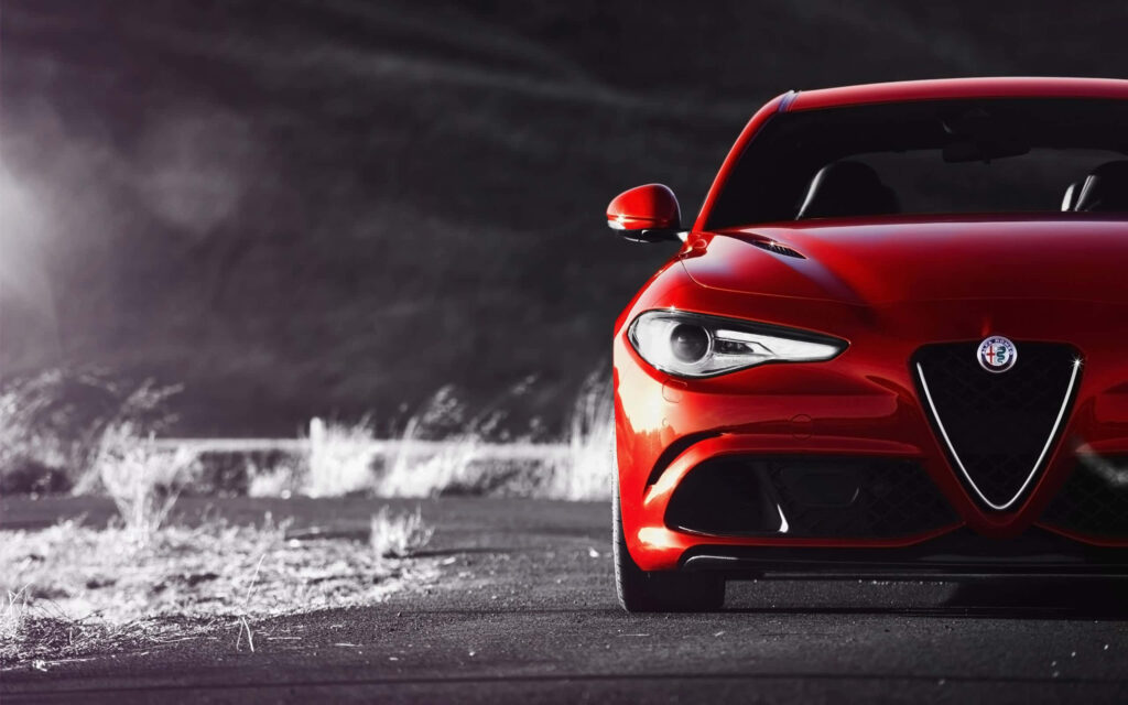Red Alfa Romeo Giulia driving on scenic road with sunlight highlighting sleek modern design Wallpaper