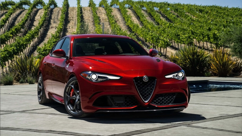 Red Alfa Romeo Giulia parked in lush green vineyard showcasing sporty design vibrant wallpaper