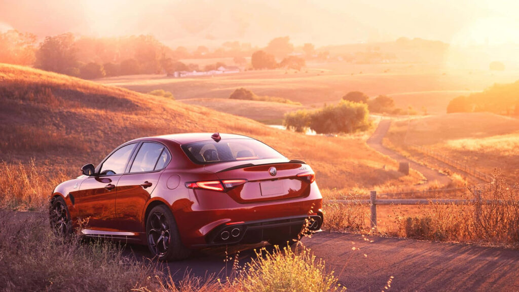 Red Alfa Romeo Giulia parked in golden countryside at sunset showcasing elegance and performance Wallpaper