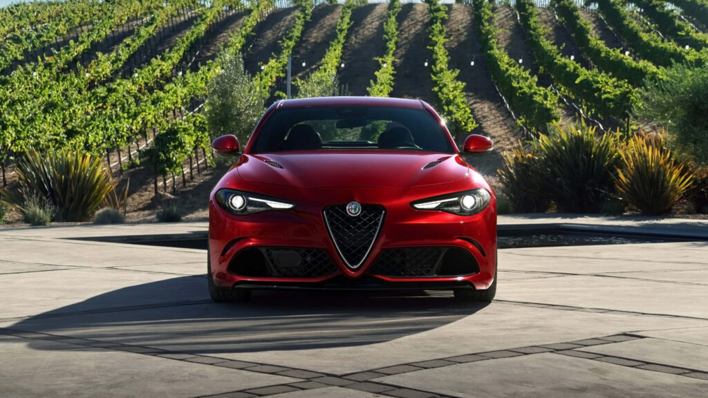 Red Alfa Romeo Giulia parked by green vineyard rows showcasing sporty Italian design outdoors Wallpaper