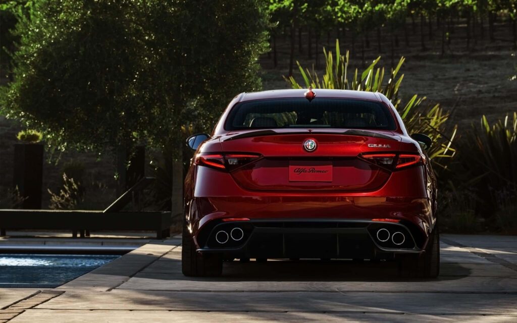 Red Alfa Romeo Giulia on scenic road surrounded by green trees and natural sunlight wallpaper
