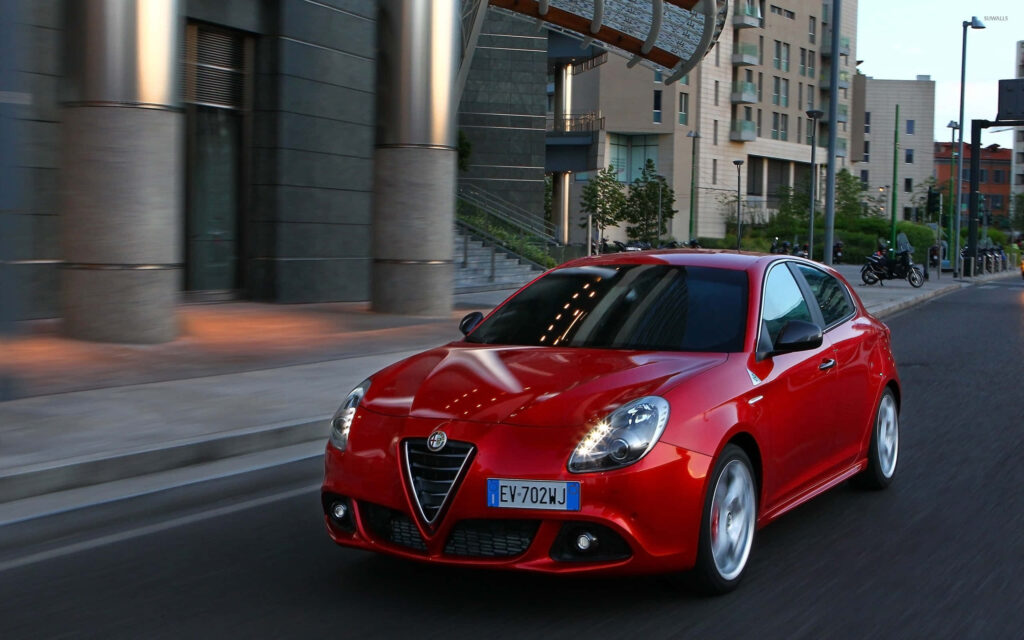 Red Alfa Romeo Giulietta speeding through vibrant modern cityscape highlighting sleek design Wallpaper