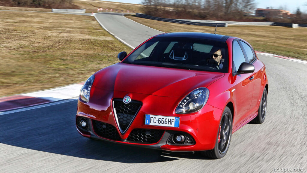 Red Alfa Romeo Giulietta speeding on scenic road with green fields and clear blue sky background Wallpaper