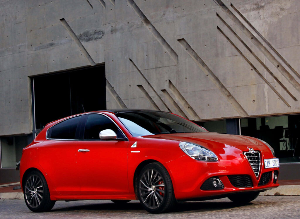 Red Alfa Romeo Giulietta parked by modern concrete wall showcasing sporty Italian design wallpaper