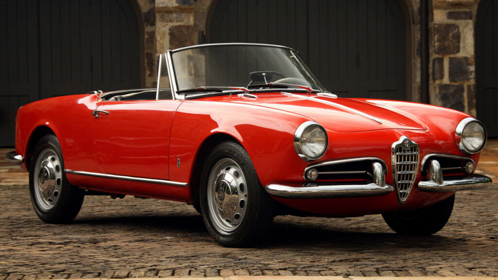 Red Alfa Romeo Spider convertible parked on cobblestone street showcasing classic Italian design Wallpaper