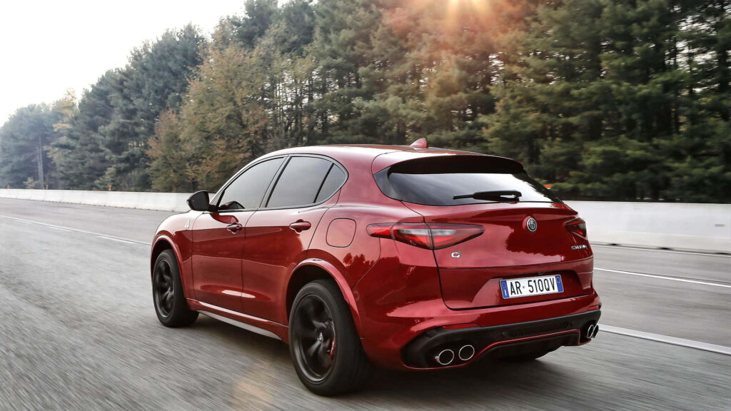 Red Alfa Romeo Stelvio driving on scenic road surrounded by lush green trees wallpaper background