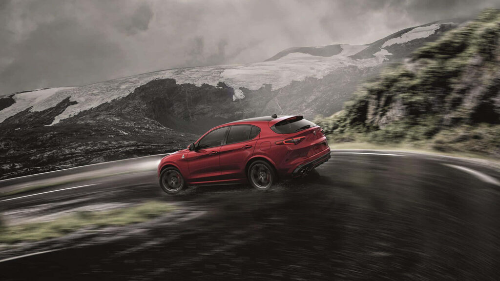 Red Alfa Romeo Stelvio speeding on mountain road under dramatic cloudy sky adventure wallpaper