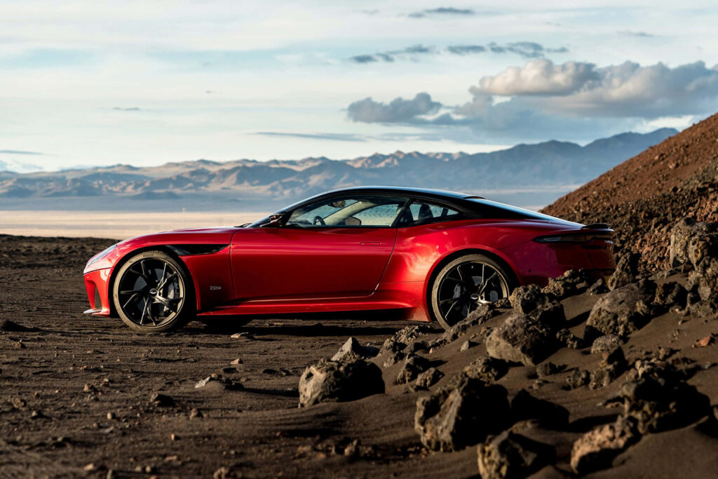 Red Aston Martin DBS Superleggera on rugged mountain road with dramatic sky wallpaper background