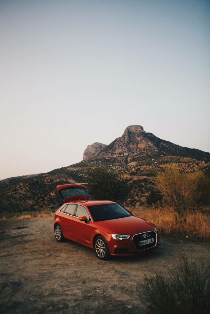 Red Audi Q5 on rugged dirt path with sunlit mountains and clear evening sky background Wallpaper