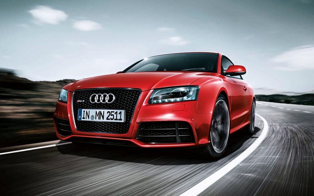Red Audi speeding on winding scenic road dynamic design powerful car wallpaper background