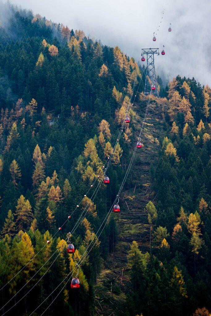 Red cable cars glide above evergreen and golden forest with misty mountain clouds wallpaper