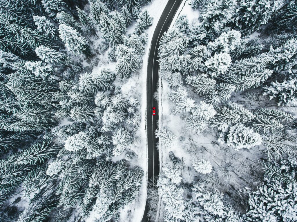 Aerial view of winding road through snow-covered forest with vibrant red car winter landscape Wallpaper