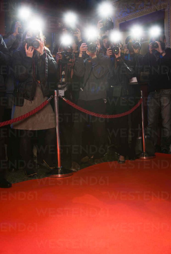 Photographers capturing bright flashes at a glamorous red carpet event with velvet ropes background Wallpaper