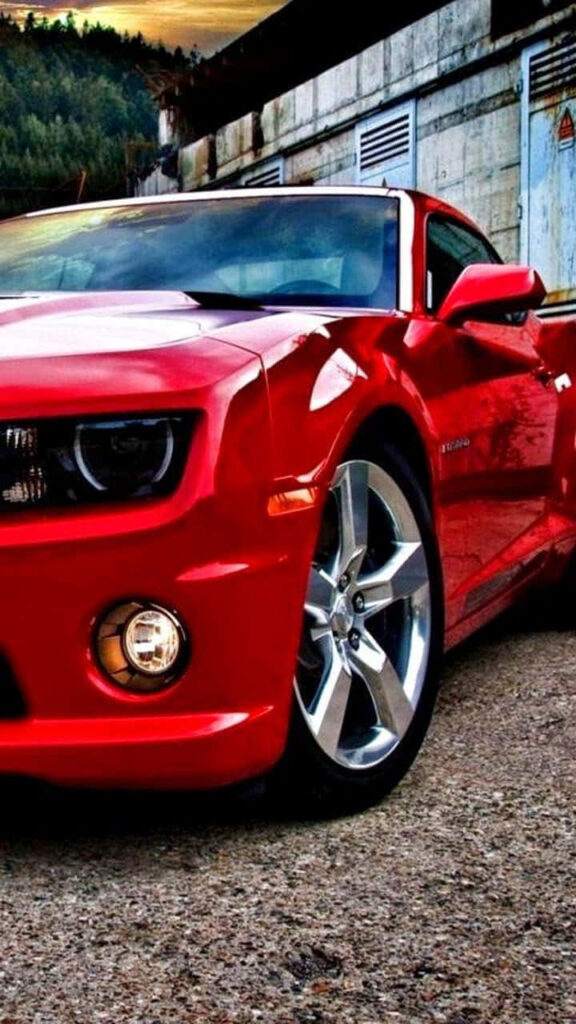Red Chevrolet Camaro parked on rugged concrete with industrial background powerful design Wallpaper