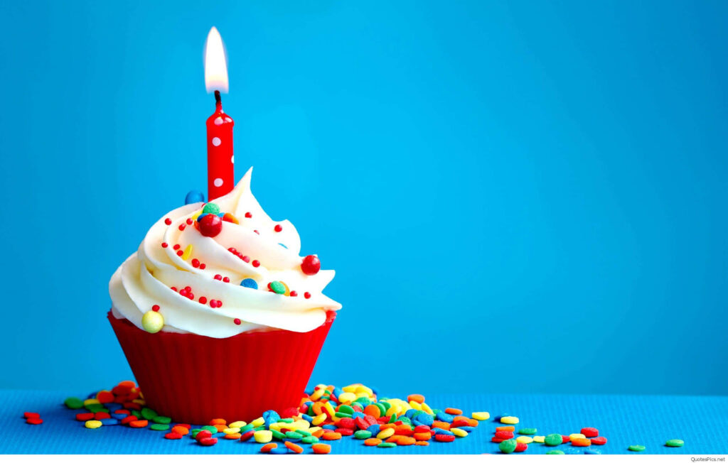 Red cupcake with white frosting colorful sprinkles lit candle on bold blue birthday wallpaper background