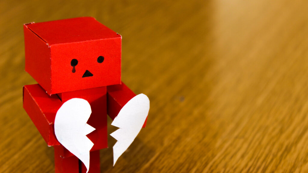 Red Danbo robot holding broken heart on wooden background with vivid colors and sharp detail Wallpaper