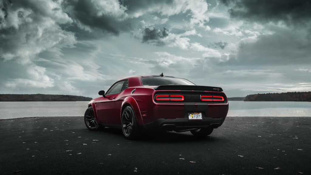 Red Dodge Challenger Demon parked by calm water under dramatic cloudy sky 4K wallpaper