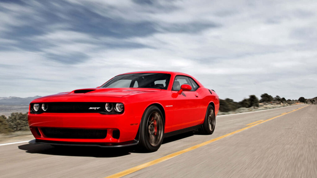 Red Dodge Hellcat speeding on open highway under dramatic skies wallpaper background