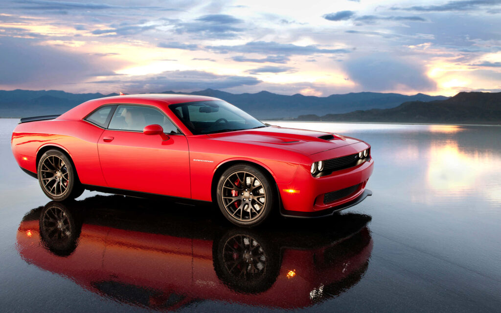 Red Dodge Hellcat parked by calm water reflecting sunset sky and powerful muscle car design Wallpaper