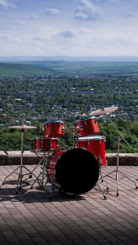 Vibrant red drum set on stone terrace with green valley and town under bright cloudy sky wallpaper