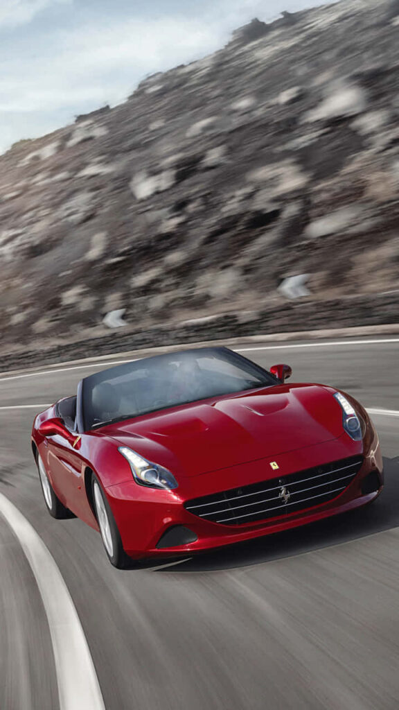 Red Ferrari California speeding on winding mountain road with dramatic rocky background wallpaper