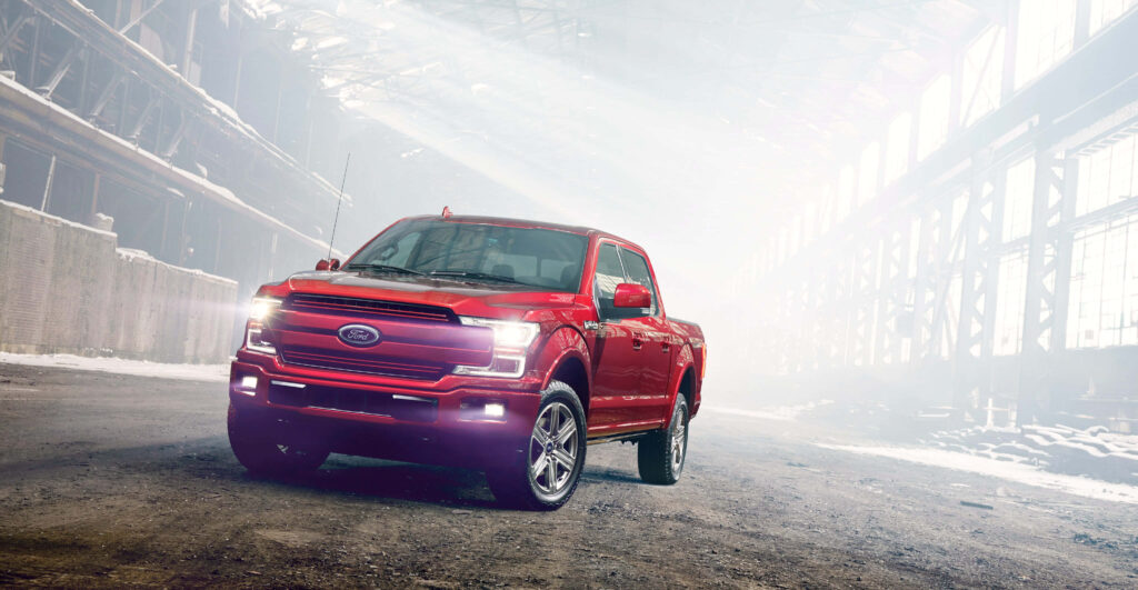 Bold red Ford F-150 truck driving inside industrial building with sunlight highlighting rugged design Wallpaper