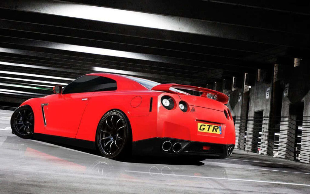 Red Nissan GTR R35 parked in dimly lit modern garage showing sleek rear design and stance Wallpaper
