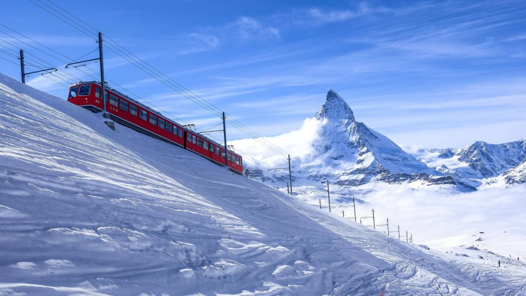 Red Gornergrat Railway train climbs snowy Swiss Alps with Matterhorn peak under clear blue sky Wallpaper