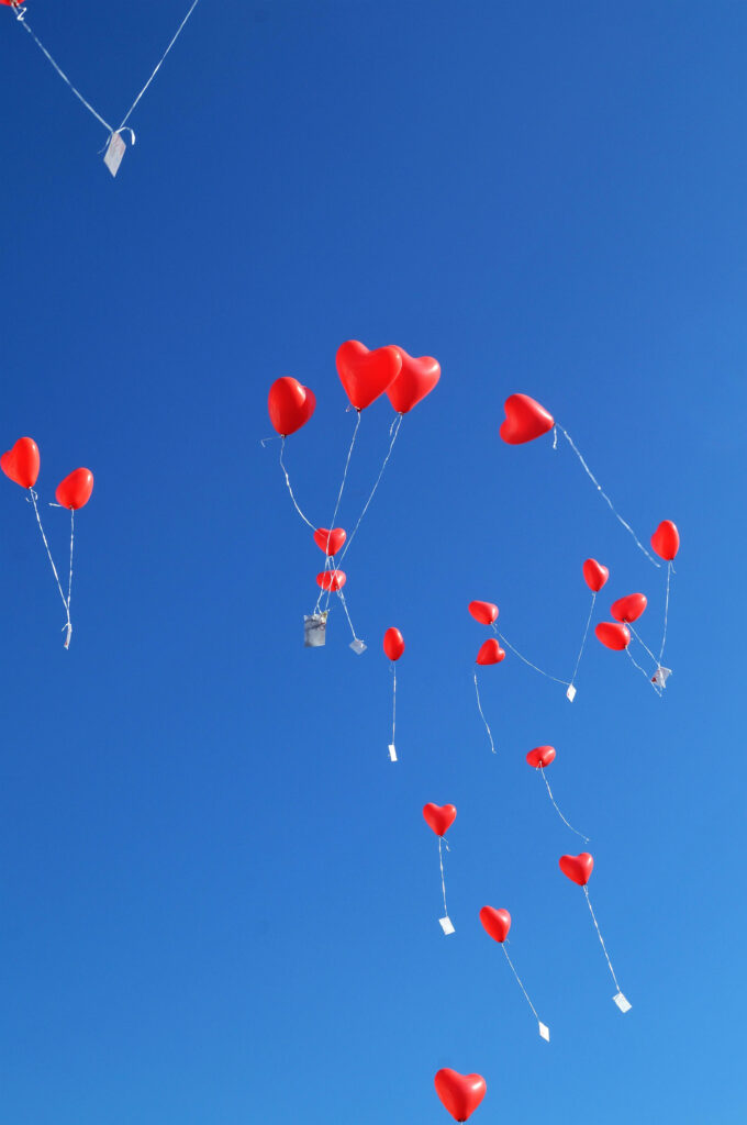 Red heart-shaped balloons floating against clear blue sky vibrant uplifting wallpaper background