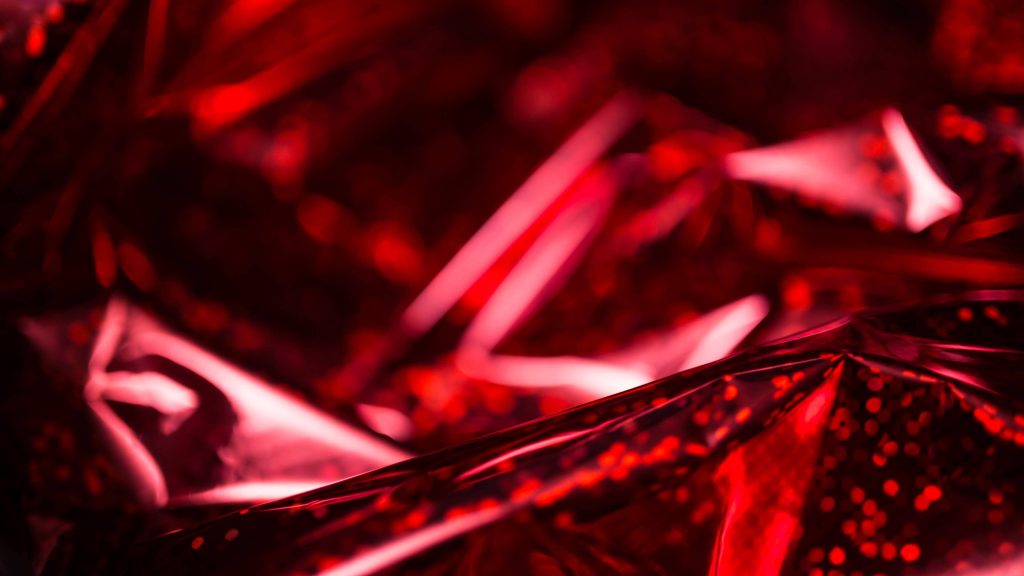 Red holographic crinkled paper wallpaper with metallic sheen and dynamic abstract texture background