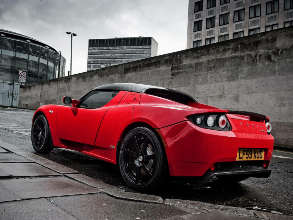 Electric Dreams: Red Tesla Roadster Rear Side View Wallpaper Against Urban Concrete Wall