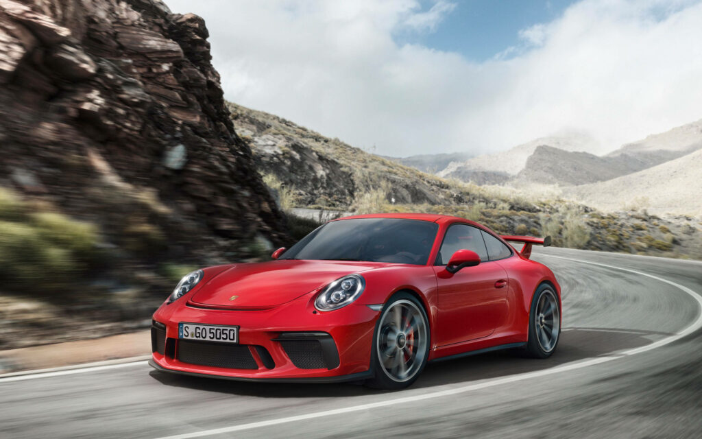The Thrilling Ride: Red Porsche 911 GT3 in Motion on Cliff Road Curve Wallpaper