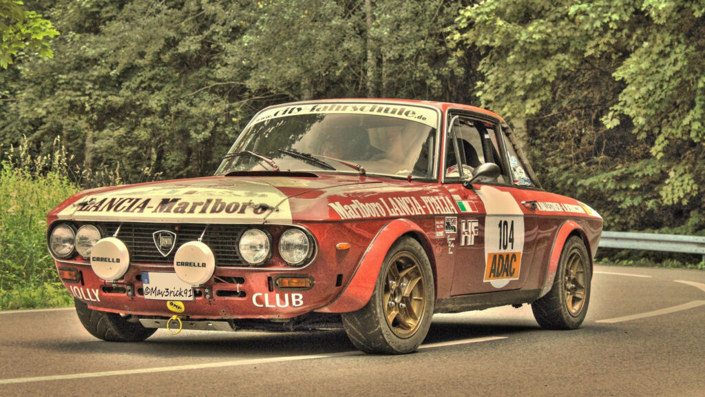 Red Lancia Fulvia classic car racing on scenic tree-lined road vintage rally wallpaper background