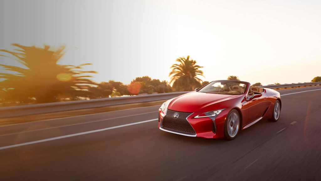 Red Lexus LC Convertible driving on palm-lined road at sunset clear sky wallpaper background
