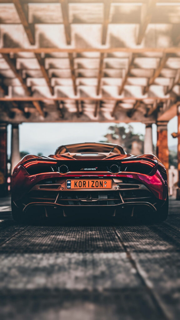 Rear view of red McLaren 720S under industrial roof with dramatic lighting sleek car wallpaper