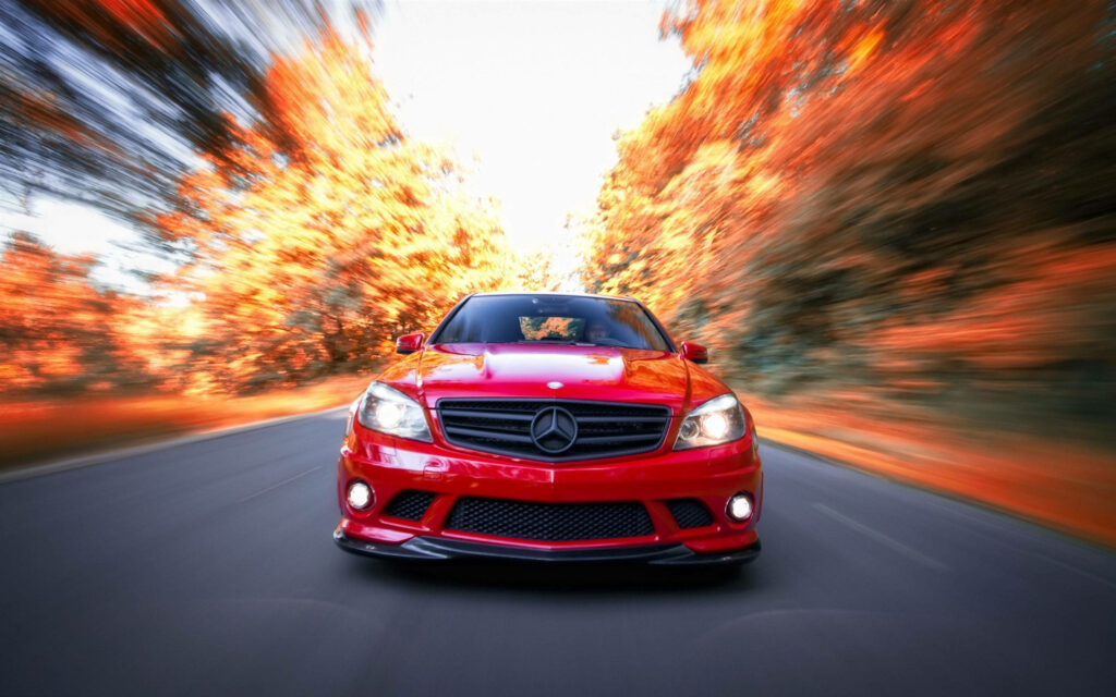 Red Mercedes AMG speeding on road with vibrant autumn trees motion blur wallpaper background