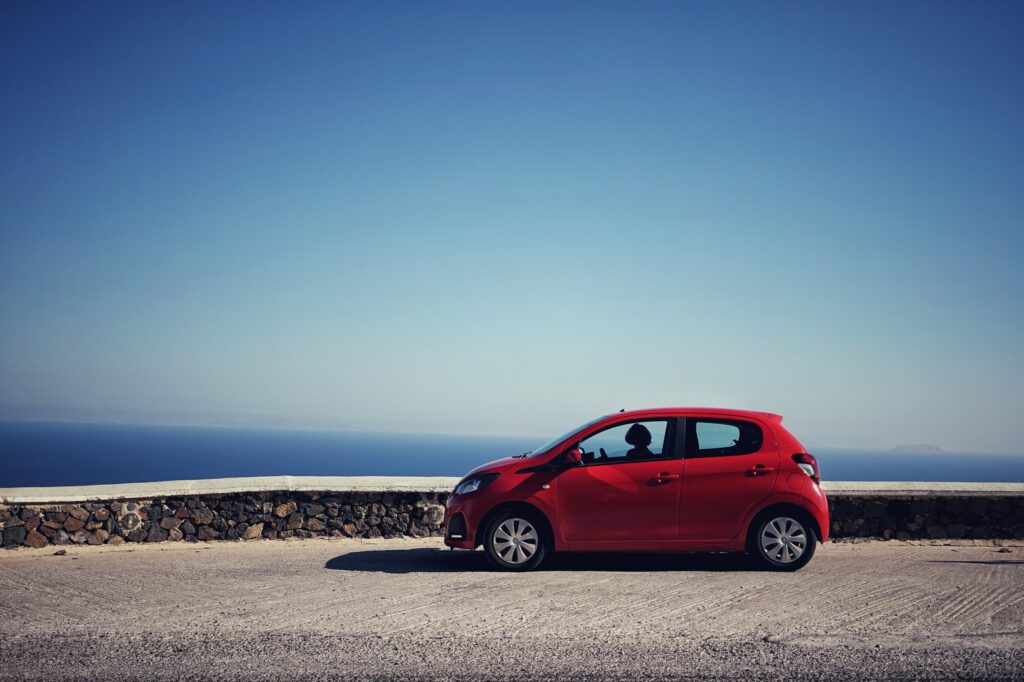 Red Mini Car in Serene Ocean Setting - Vibrant Wallpaper Background