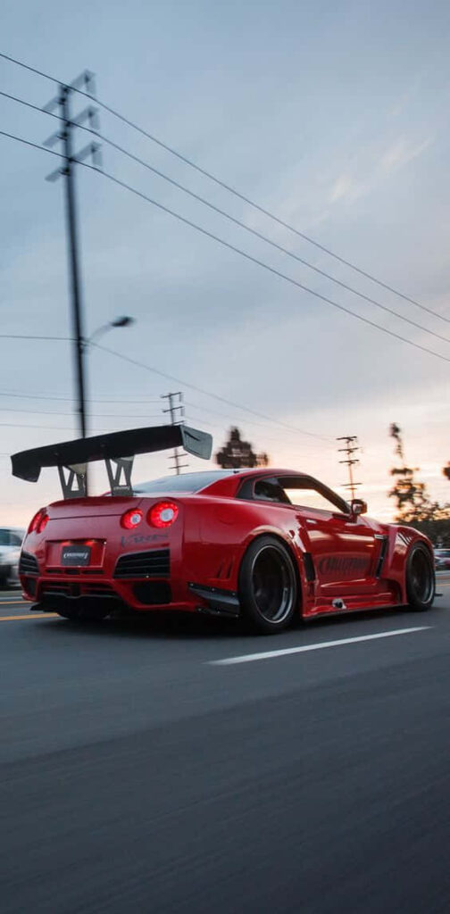Red Nissan R35 GTR with aggressive wing racing at dusk showcasing Japanese sports car power Wallpaper