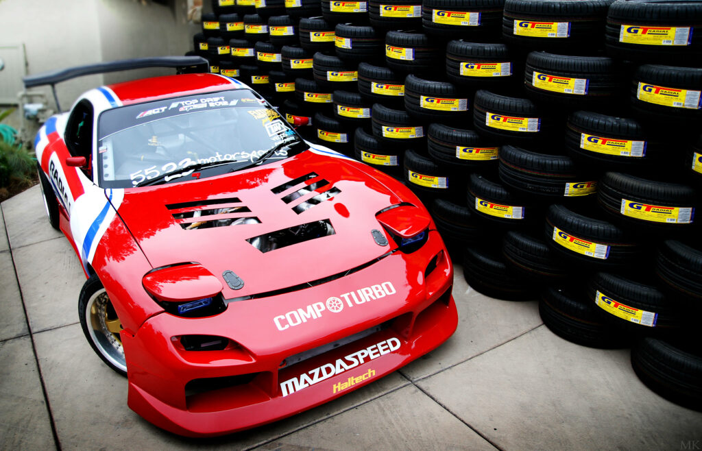 Speed Demon Resting Beside Tire Mountain: Magnificent Rx-7 Revs Up Excitement! Wallpaper