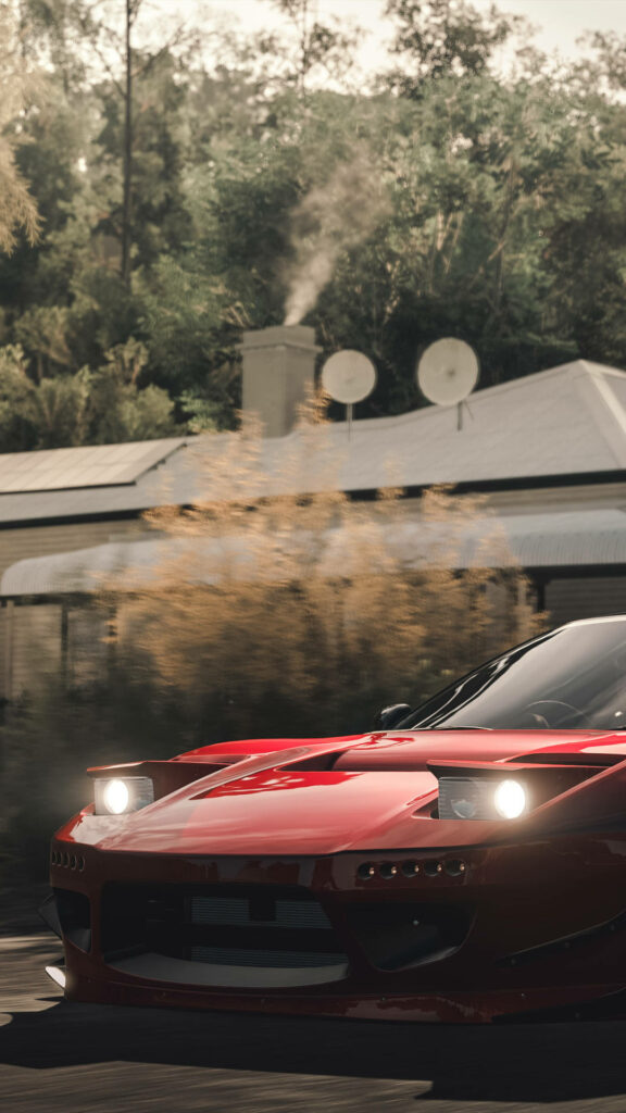 Red sports car with headlights on speeding past green trees and rustic house wallpaper background