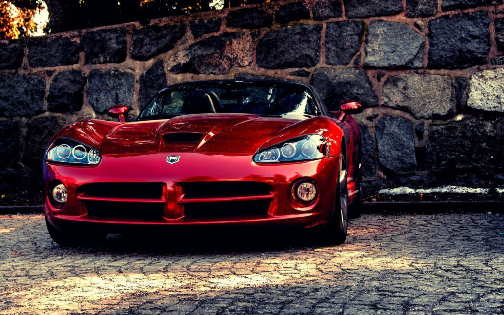 Red sports car parked on cobblestone street against rustic stone wall background wallpaper