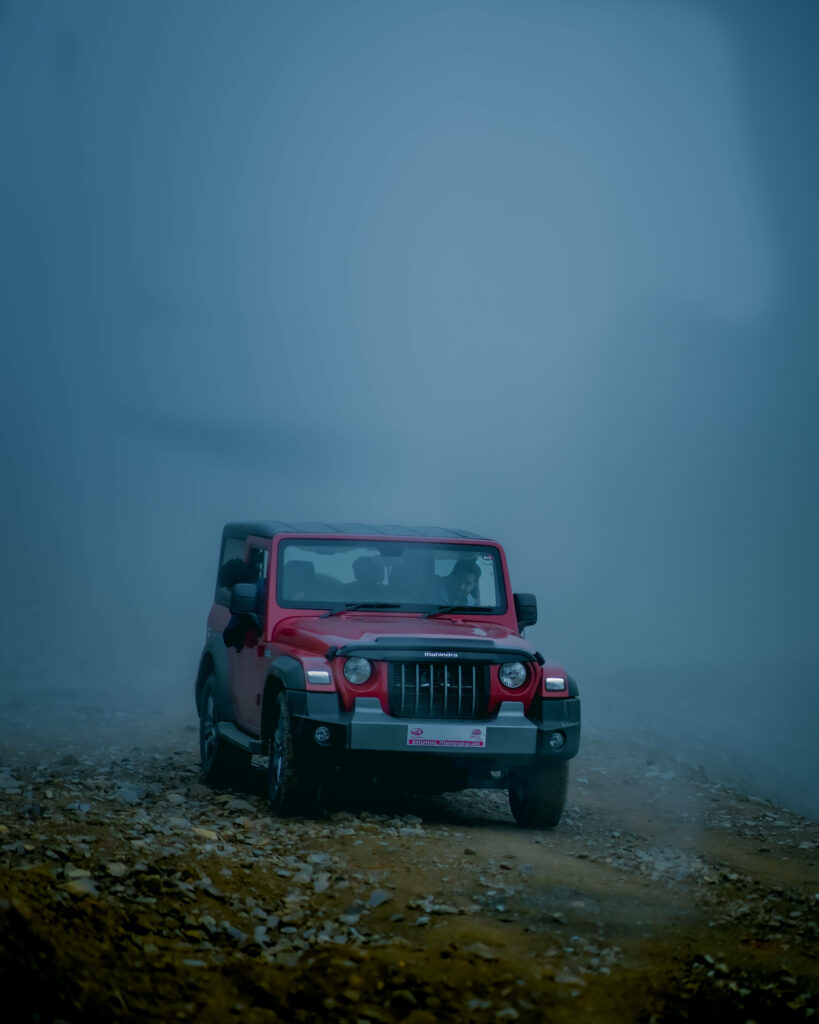 Red Thar SUV emerges through dense blue fog dramatic adventure 4K wallpaper background