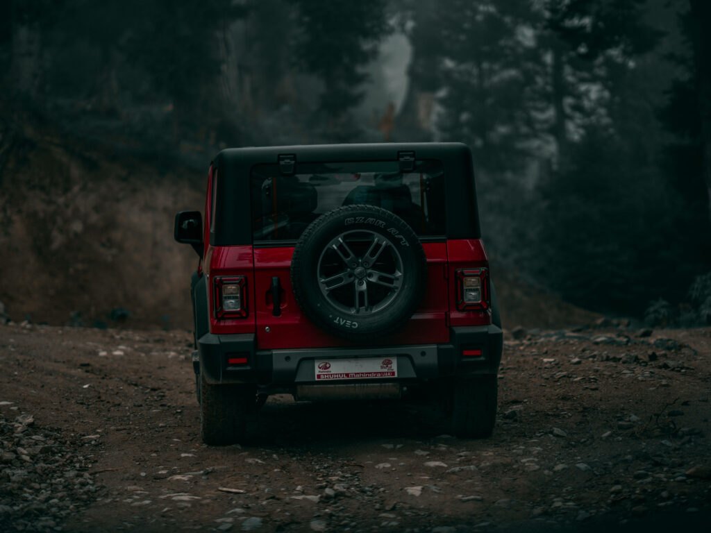 Red Thar SUV parked on rugged dirt path with dense green trees in misty forest 4K wallpaper