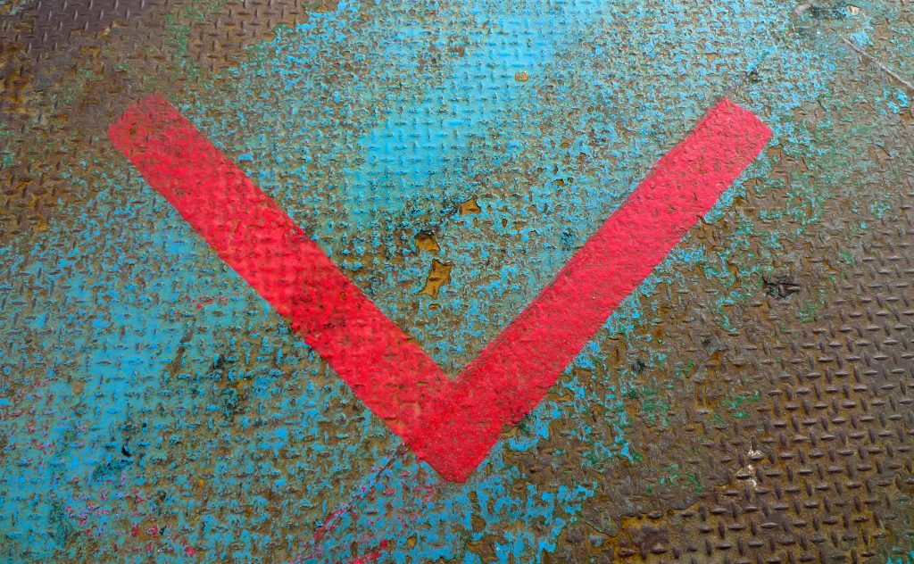Bold red V on weathered industrial metal diamond plate with rust and peeling blue paint background Wallpaper