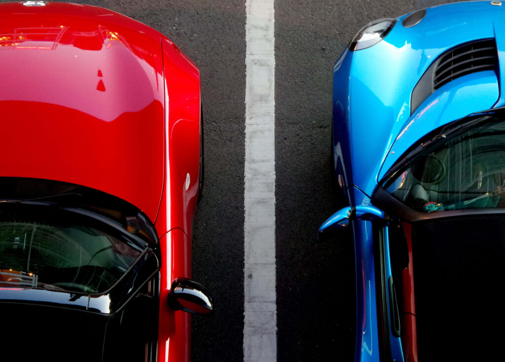 Top-down view of red and blue cars parked side by side separated by white line on asphalt Wallpaper