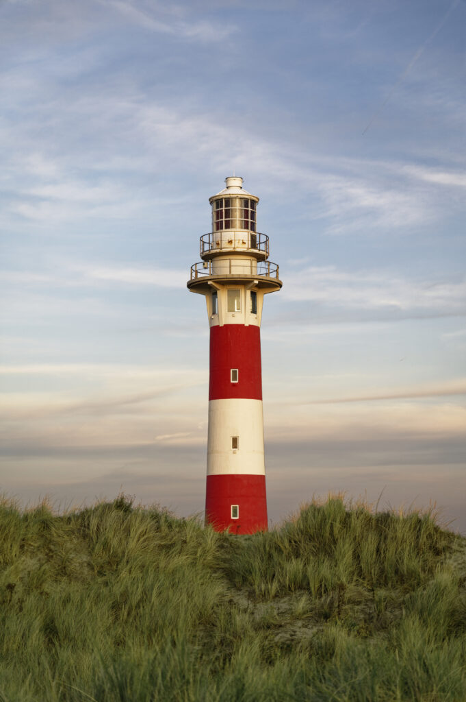Red and white striped lighthouse above green grass under peaceful sky with soft clouds wallpaper