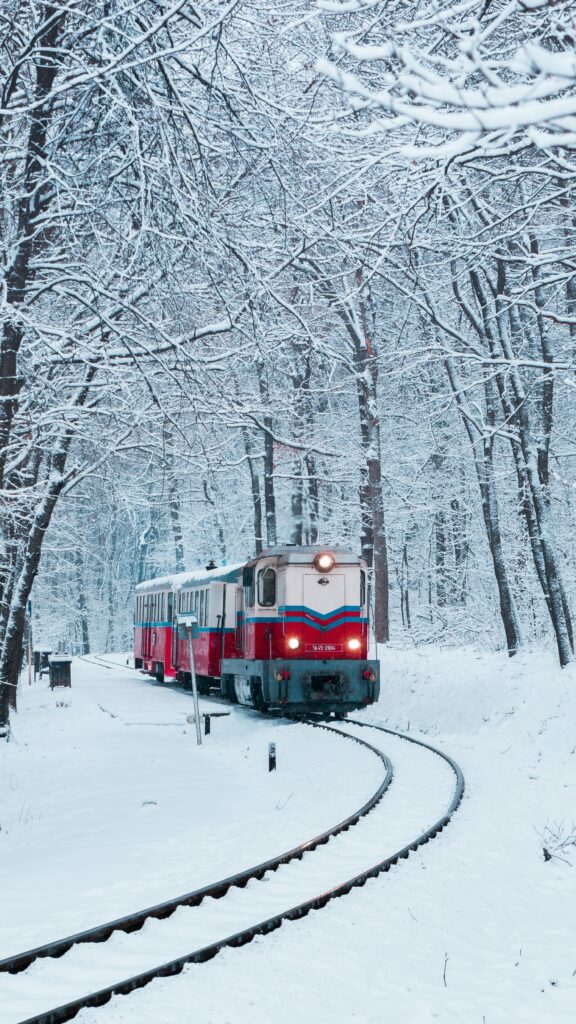 Red and white train curves through snow-covered forest with frosty trees in peaceful winter scene Wallpaper
