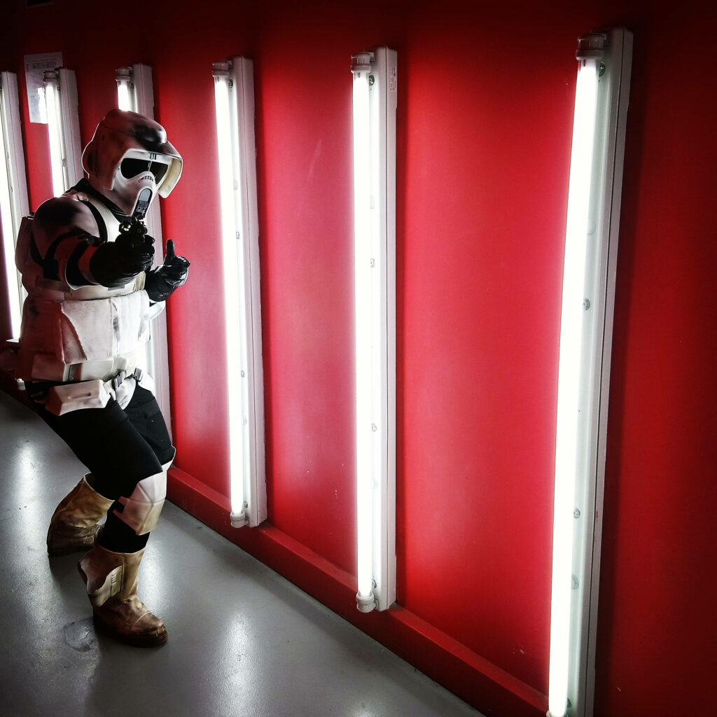 Clone Trooper in red-accented armor stands by vivid red wall with vertical white lights sci-fi wallpaper